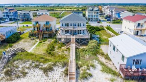 Une propriété située en bord de mer, avec une maison principale dotée d’une terrasse et d’un escalier menant à la plage.