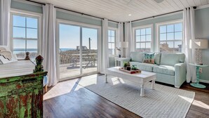 Ein geräumiges Wohnzimmer mit großen Fenstern, einer grünen Akzentwand, einem weißen Couchtisch und einem hellblauen Sofa.