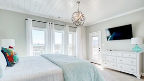 A bedroom with a bed, a TV, a dresser, and a view of the outside. - Spacious Luxe Home|Private Pool/Hot Tub (North Topsail Beach)