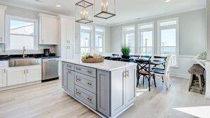 A modern kitchen with white cabinetry, a large island, stainless steel appliances, and pendant lighting. - Spacious Luxe Home|Private Pool/Hot Tub (North Topsail Beach)