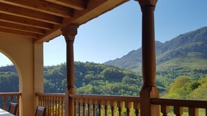 Un balcón de madera con vistas a colinas y montañas verdes.