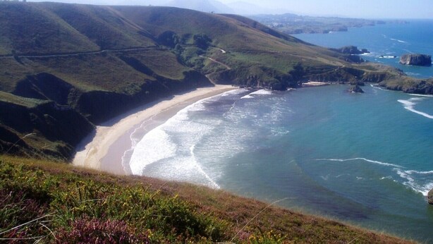 Un paisaje costero con una playa, colinas onduladas y una vista despejada del océano.