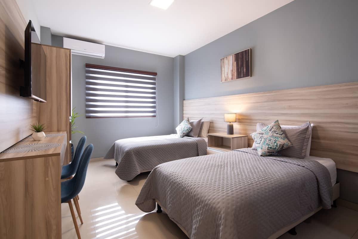 A modern bedroom with two beds, a desk, and a TV.