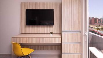 Une chambre moderne avec un téléviseur fixé au mur, un bureau, une chaise jaune et un lit recouvert d’une couverture bleue.