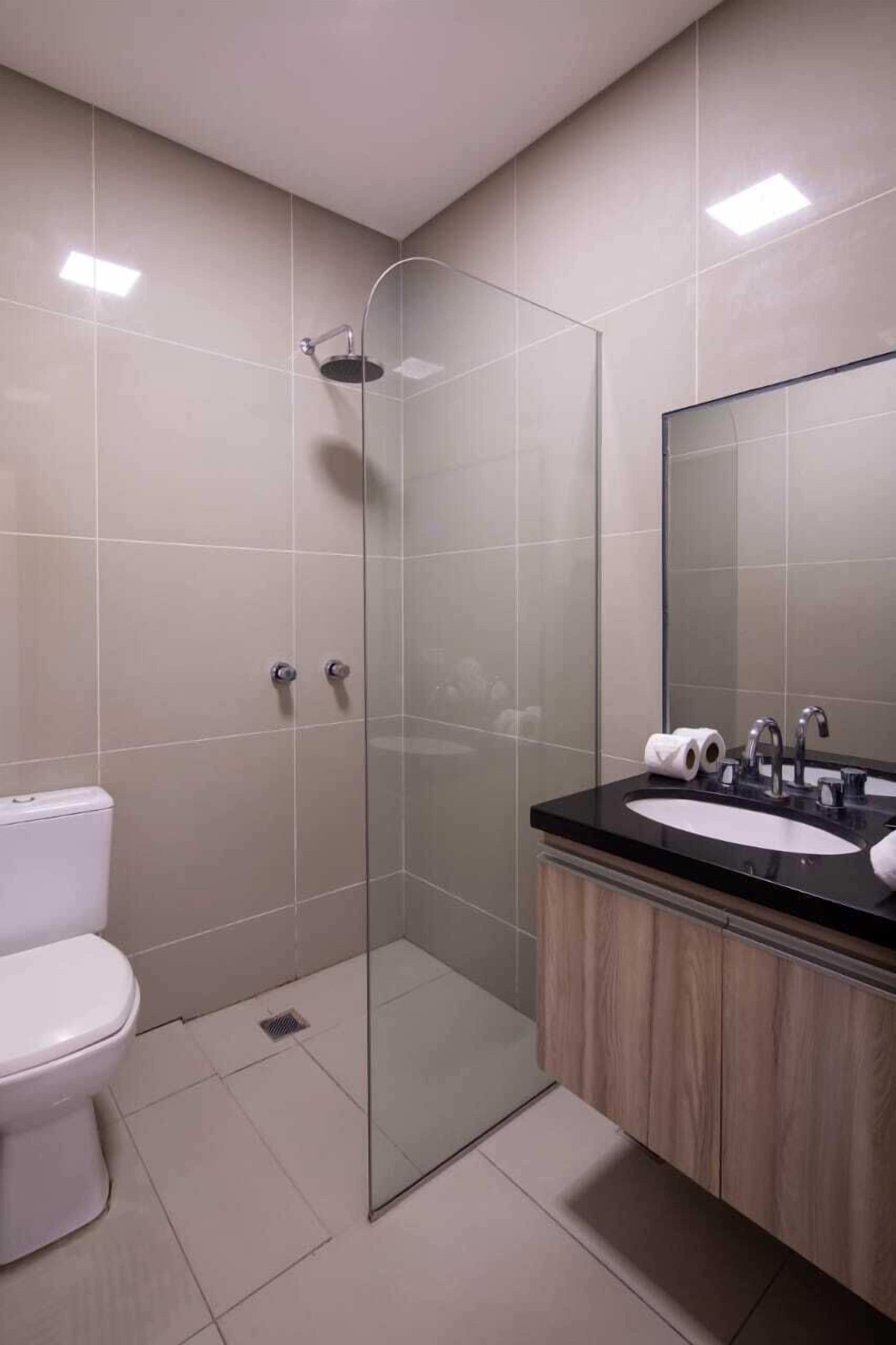 A modern bathroom with a glass-enclosed shower, a white toilet, and a wooden vanity with a mirror.
