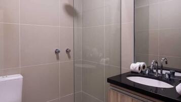 A modern bathroom with a glass-enclosed shower, a white toilet, and a wooden vanity with a mirror.