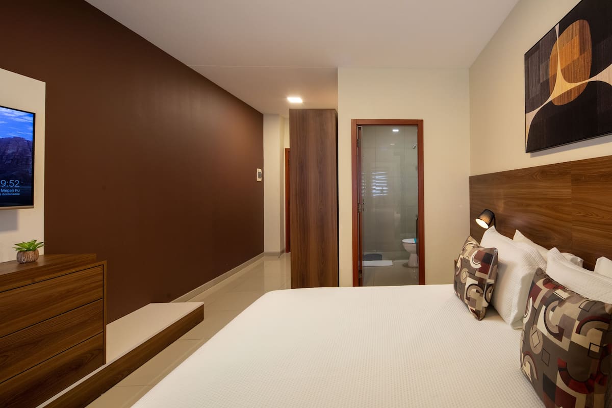 A hotel room with a bed, a wooden dresser, a TV, and a painting on the wall.