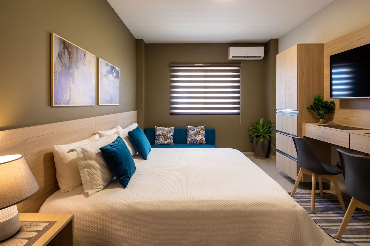 A hotel room with a large bed, a desk with a chair, a TV, and artwork on the wall.