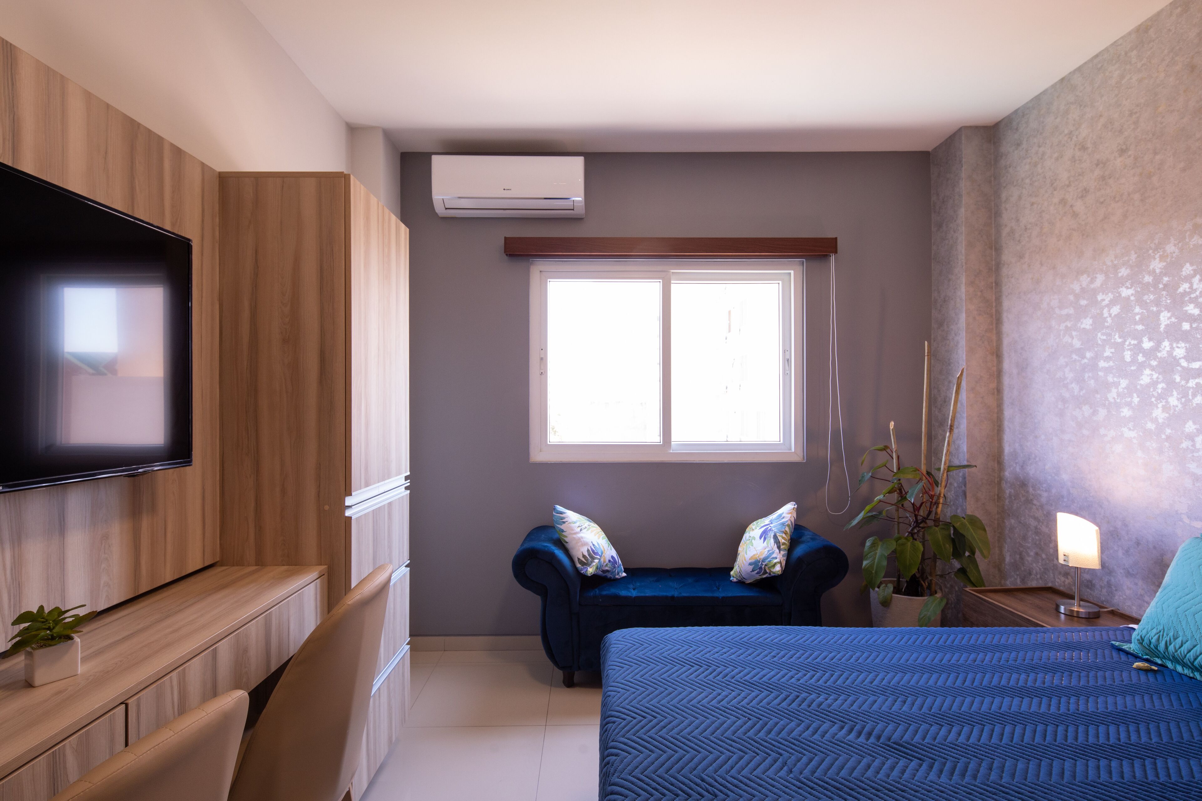 Un dormitorio moderno con una cama grande, un televisor montado en la pared, una ventana y una planta.
