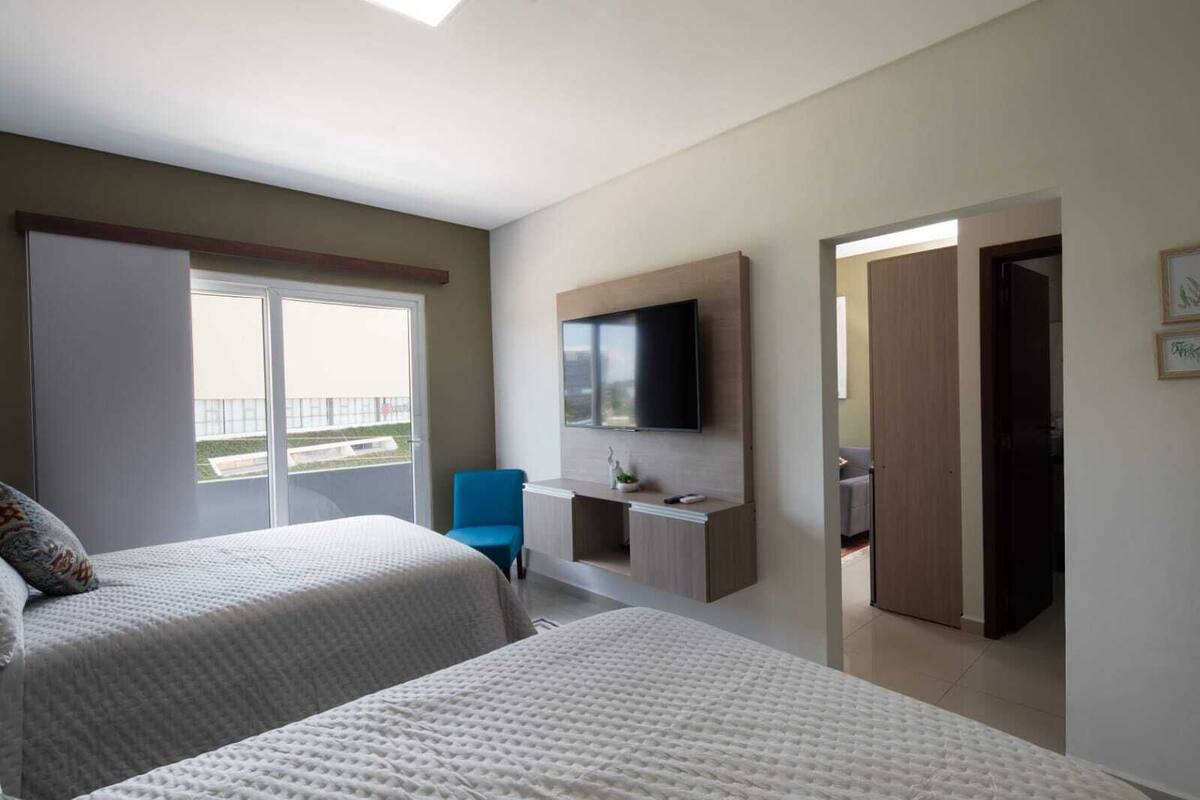 A hotel room with two beds, a TV mounted on the wall, a desk, and a chair.