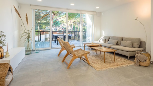 A modern living room with a sofa, two wicker chairs, a coffee table, and a large sliding glass door leading to an outdoor area with a balcony. - Newly built house with private pool (Begur)