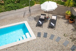 Un espace piscine aménagé sur le toit, avec des chaises longues, un parasol blanc et des plantes en pot.