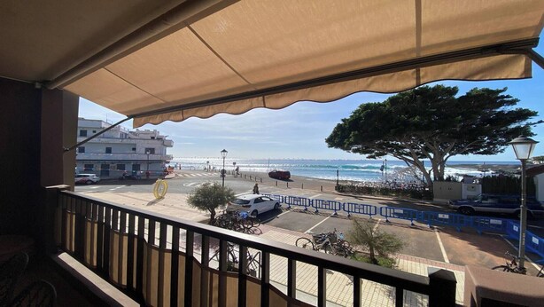 Uma varanda com vista para a praia e o oceano, um carro estacionado e uma bicicleta.