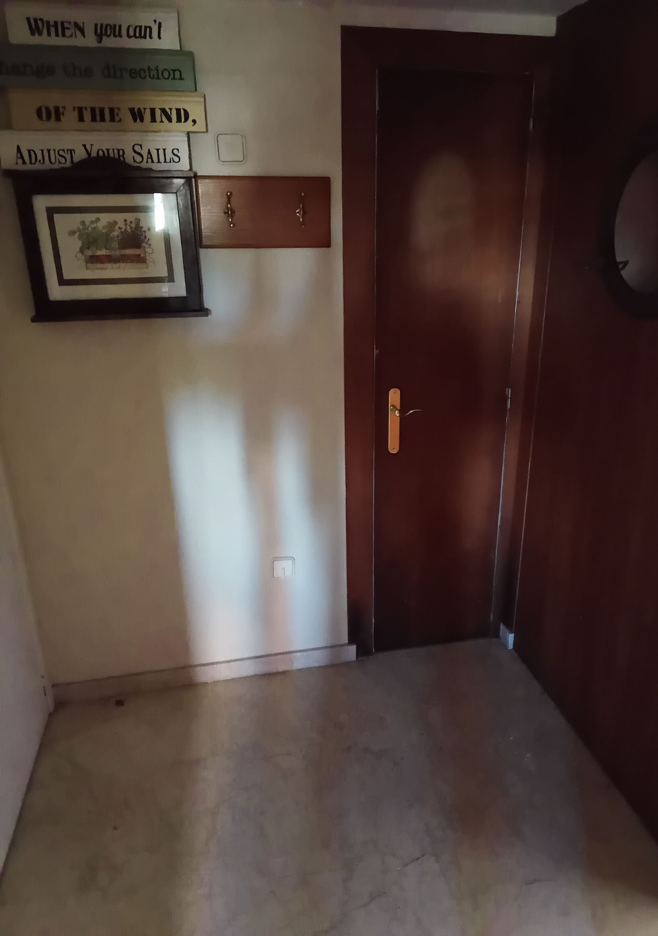 A hallway with a wooden door, a framed picture, and a sign on the wall.