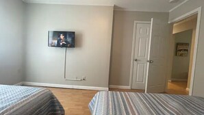 Un dormitorio con dos camas, un televisor montado en la pared y una puerta que da a otra habitación.