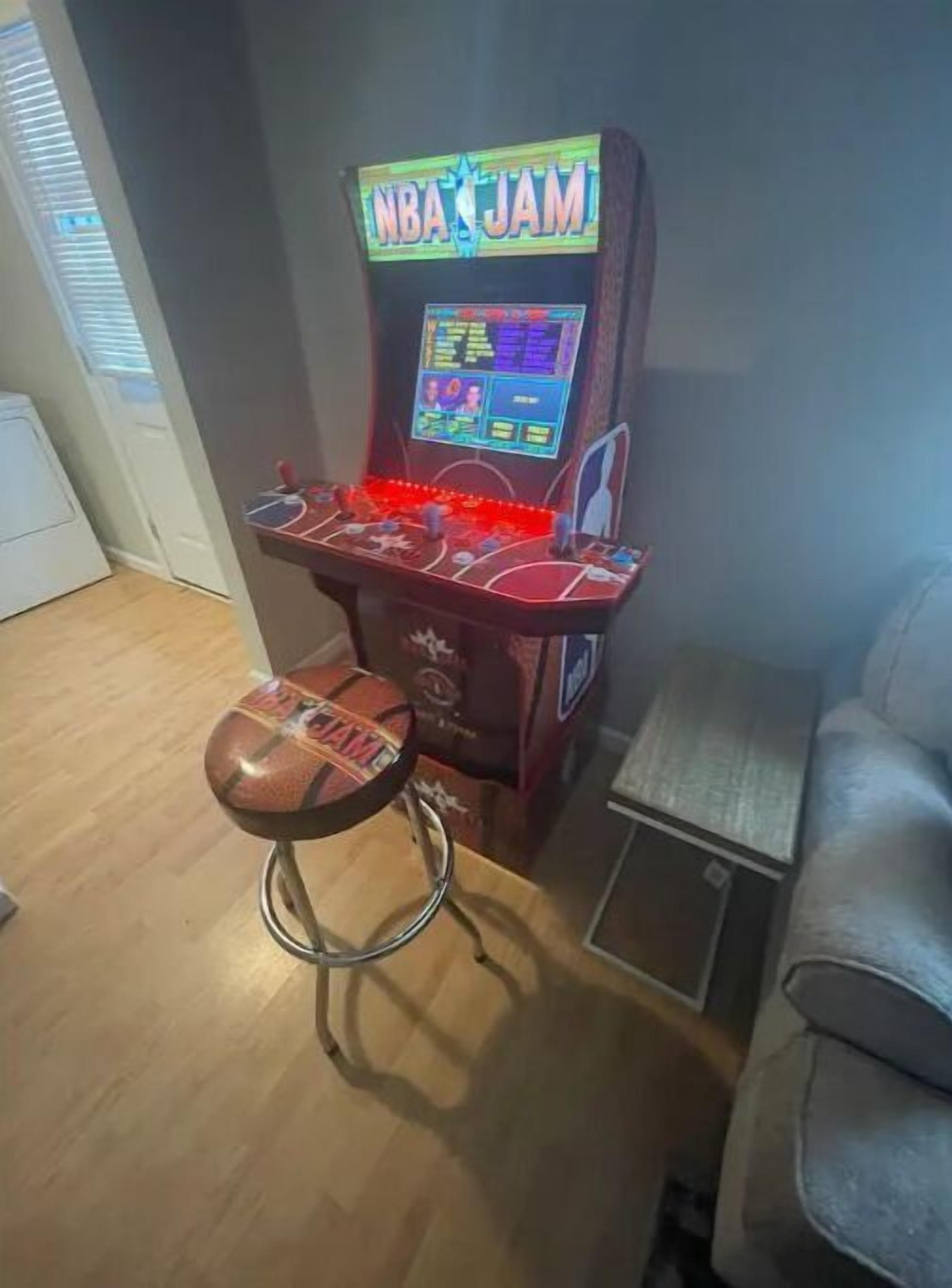 An arcade machine labeled "NBA JAM" with a basketball-themed stool.