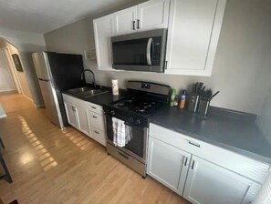 A modern kitchen with white cabinets, a stainless steel refrigerator, a microwave, a stove, and a sink.