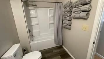 Un baño con inodoro, ducha y bañera. Hay toallas apiladas en la pared.
