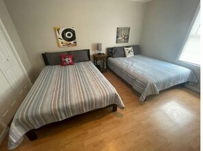 A bedroom with two single beds, wooden flooring, a small bedside table with a lamp, and wall art.