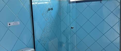 A bathroom with a glass-enclosed shower, a toilet, and a window with stained glass.