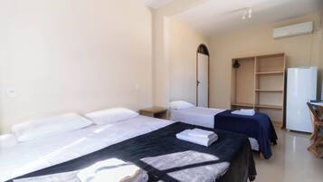 A hotel room with two single beds, a desk, a chair, a wardrobe, and a refrigerator.