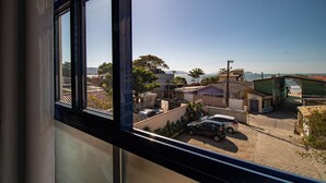Ein Wohngebiet mit Häusern, parkenden Autos und freiem Blick auf den Ozean durch ein Fenster.