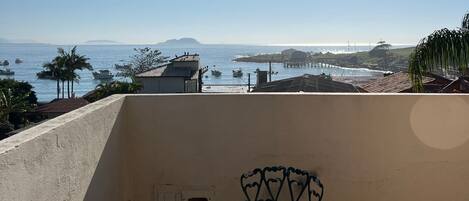 Un balcone con tavolo e sedia, affacciato su una vista costiera con barche e terra in lontananza.