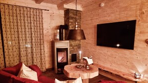 Un accogliente soggiorno con un divano rosso, un camino, una TV a muro e un soffitto in legno.