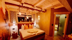 Una camera da letto accogliente con soffitto in legno, un letto grande con molti cuscini, lampade sui comodini e una finestra con tende.