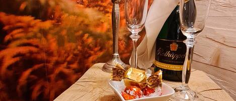 A wooden table with a bottle of wine, two wine glasses, a candle, and a plate of chocolates.