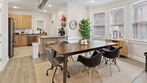 Una cocina moderna con armarios de madera, un refrigerador de acero inoxidable y un comedor con una mesa de madera oscura y sillas negras.
