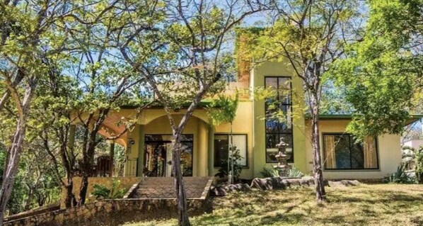 Uma casa de dois andares com base de pedra, fachada amarela e pequena varanda frontal.