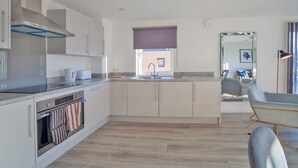 A modern kitchen with white cabinets, a built-in oven, and a window with a blind. - Contemporary 2 Bedroom Apartment in Ashford (Ashford)