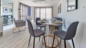 A modern dining area with a round table, grey upholstered chairs, and a gold-framed base. - Contemporary 2 Bedroom Apartment in Ashford (Ashford)