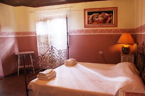 A bedroom with a bed, a bedside table, a lamp, a painting on the wall, and a window with a curtain.