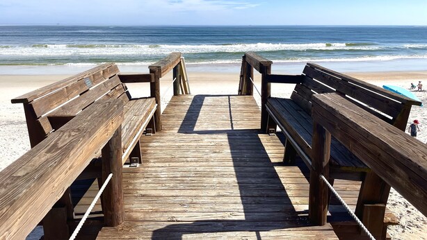 Una pasarela de madera que lleva a una playa con bancos y una vista despejada del océano.