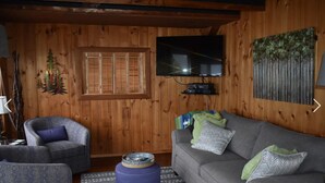 Un salon chaleureux avec des murs en bois, un canapé gris, un fauteuil bleu et un petit pouf.