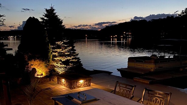 Un espace extérieur aménagé pour les repas, avec un barbecue, des sièges et une vue sur un lac au crépuscule.
