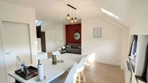 A modern kitchen with a central island, white bar stools, pendant lighting, and a red accent wall.