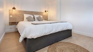 A modern bedroom with a wooden headboard, two bedside lamps, a bed with white linens, and a woven rug on the floor.