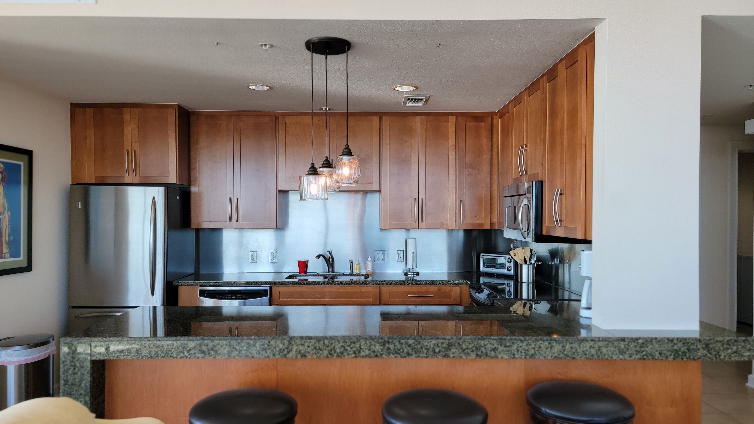 A modern kitchen with wooden cabinets, stainless steel appliances, granite countertops, and pendant lighting.