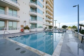 Une piscine située à côté d’un immeuble à plusieurs étages, doté de balcons et de grandes fenêtres.