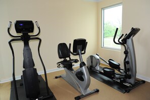 Three stationary bikes in a room with beige walls and a window. - Ocean Club 805 Deluxe | Stunning Panoramic Views of the Gulf! (Biloxi)