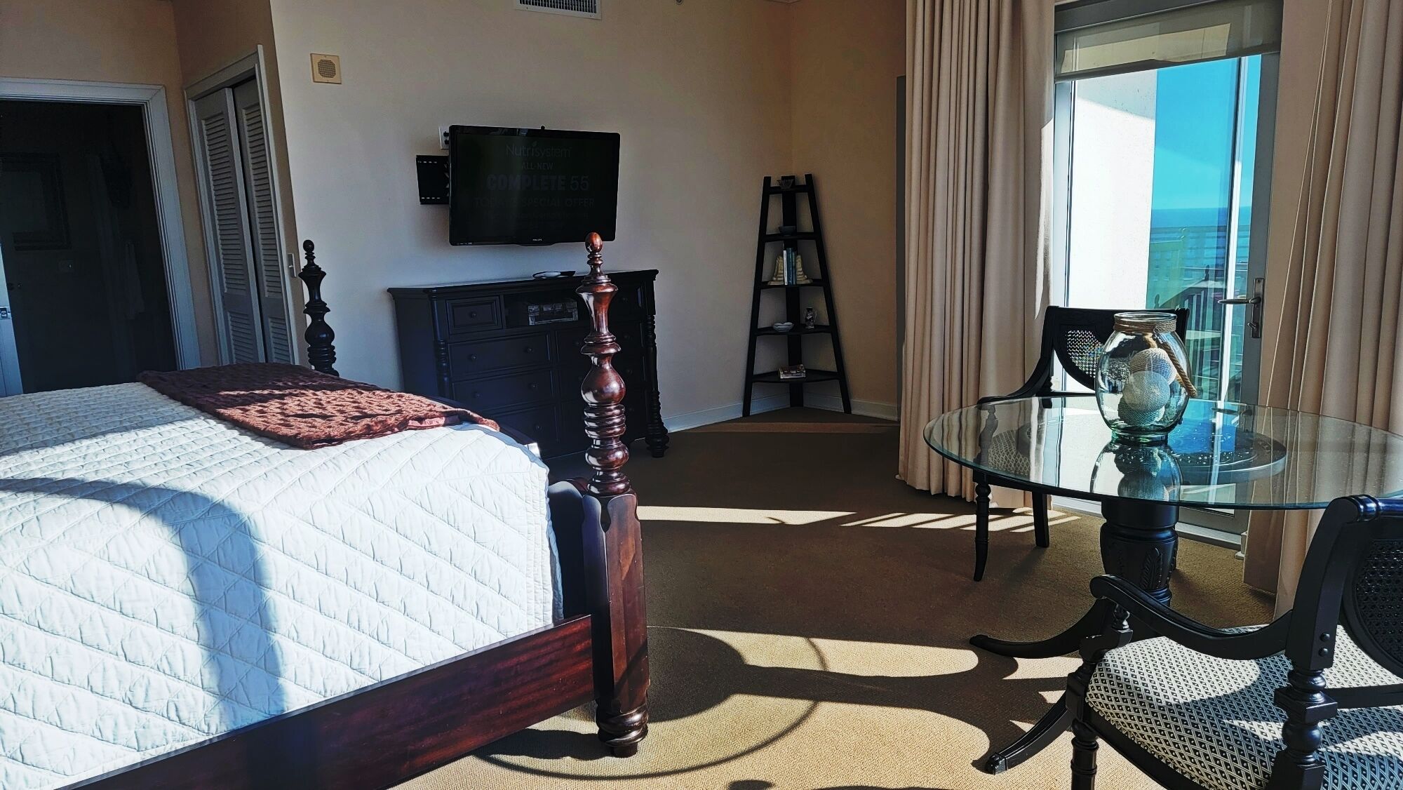 A hotel room with a bed, a television, a desk with a chair, and a view of the ocean.