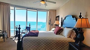 Une chambre d’hôtel avec un grand lit, une vue sur l’océan, un ventilateur de plafond et une table avec une lampe.