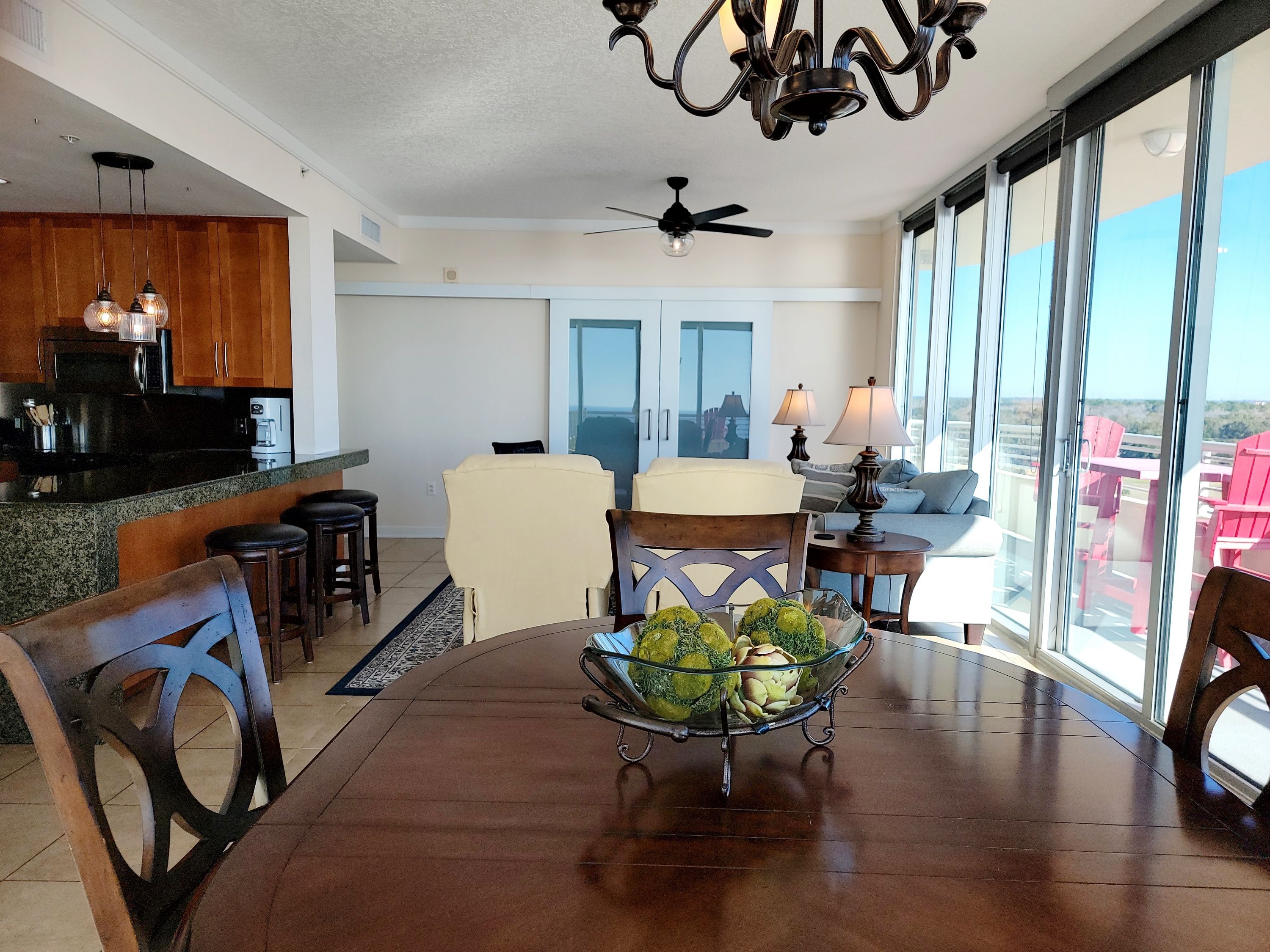 A dining area with a table, chairs, and a centerpiece of green vegetables. There is a kitchen area with cabinets and appliances in the background. - Ocean Club 805 Deluxe | Stunning Panoramic Views of the Gulf! (Biloxi)