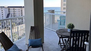 Een balkon met uitzicht op de oceaan, met twee houten stoelen en een bijzettafeltje met een bloempot.