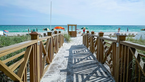 Een houten looppad dat naar een strand leidt, met parasols en een redderspost.