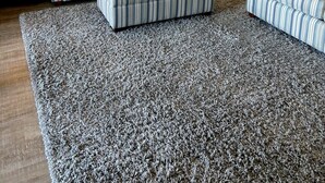Een woonkamer met gestreepte banken, een salontafel en een vloerkleed. Achtergrond: een keuken met witte kasten.