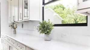 Una cocina moderna con armarios blancos, encimera de mármol y ventana con vistas a la vegetación.
